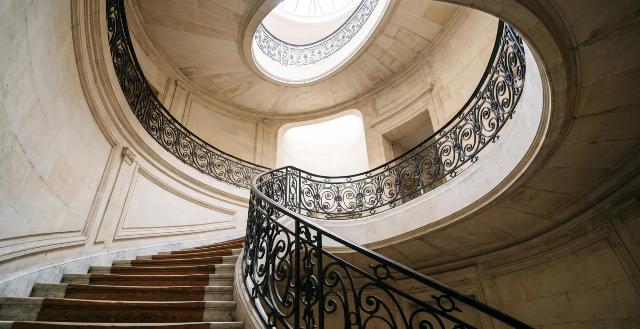 Escalier en colimaçon de style haussmannien menant vers une lumière naturelle, symbolisant l'ascension d'une page web vers le top 3 de Google et la conversion